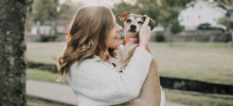 smiling-woman-carrying-dog-near-tree