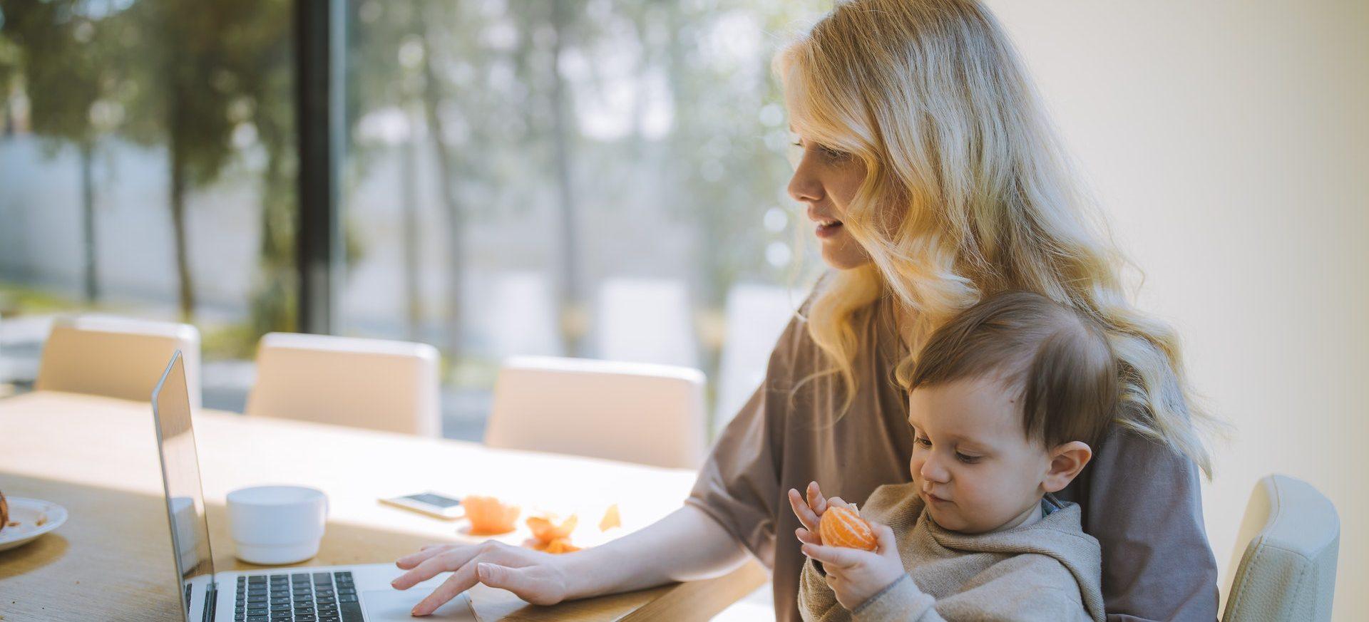 A woman holding her baby filling out an online form.