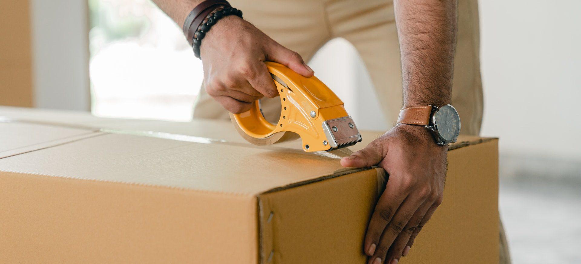 A man duct taping a moving box shut.