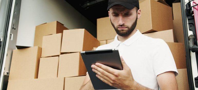 A man in front of moving boxes checking something on his papers.