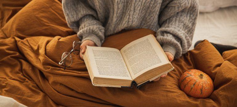 Mujer de suéter con un libro en las manos, sentado debajo de la manta