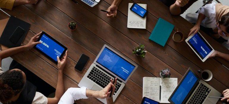 people sitting and leaning on a wooden table while typing on laptops and tablets 