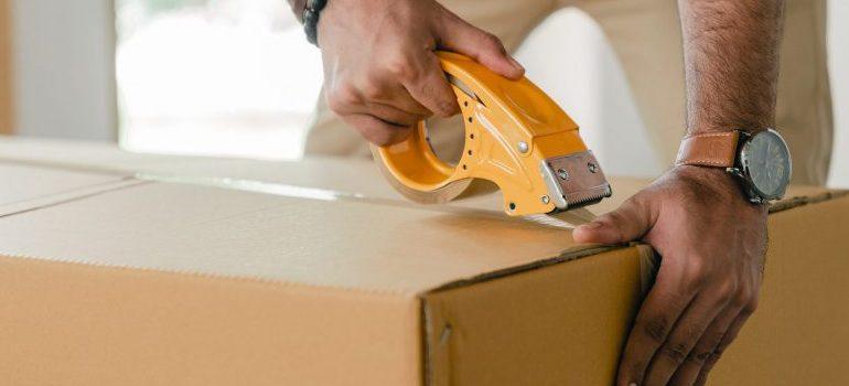 person sealing a packing box with tape