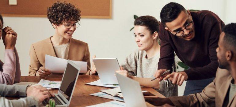 people in the office sitting around the table using laptops and papers