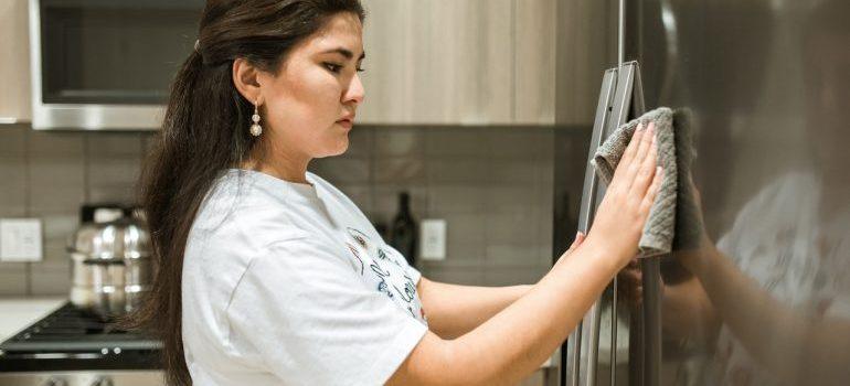 a woman in white t-shirt wiping the door of the fridge