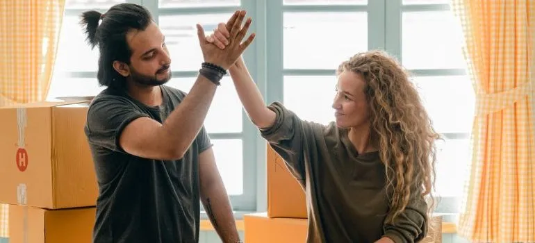 A man and a woman giving each other a high-five while next to a closed cardboard box representing things to make your NYC moving day more enjoyable