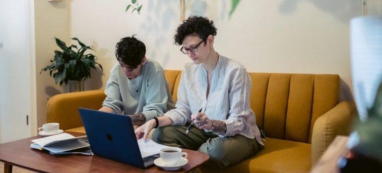 Dos personas sentadas en un counch doind de investigación en un portátil con cuadernos o la mesa de al lado que representa la adaptación después de mudarse a Sugar Land