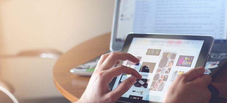 Hands holding tablet in front of the laptop screen before the time comes to pack electronic devices before the move. 