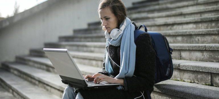 Una chica sentada en las escaleras de la lectura en su computadora acerca de cómo prepararse para la mudanza a nueva york como estudiante