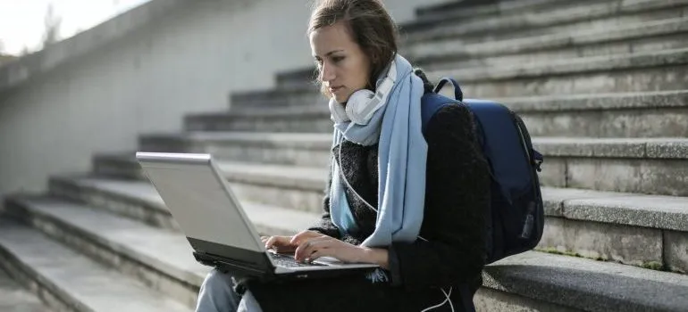 A girl sitting on the stairs reading on her laptop about how to prepare for moving to NYC as a student