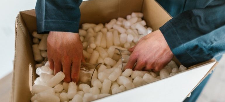 Person packing glasses in a cardboard box.