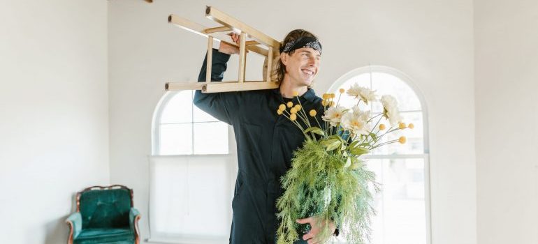 A smiling mover carrying a plant and a chair