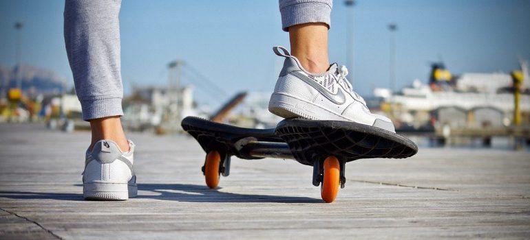 The girl's legs in sneakers and tracksuits, with one foot on the skyboard and the other on the concrete.