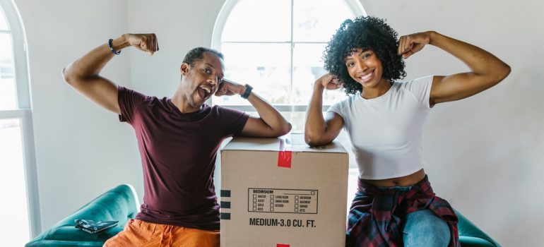 A man and woman flexing on top of a movinh box