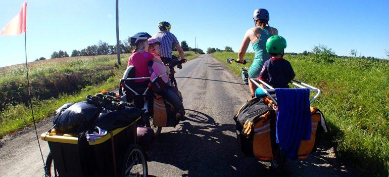 Parents and children ride bicycles with trailers.