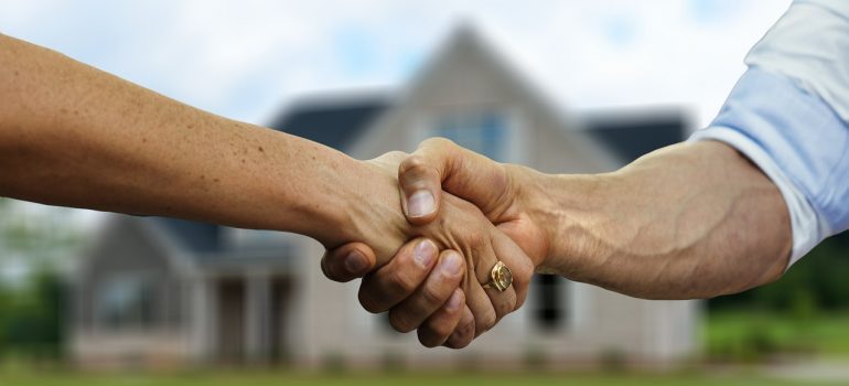 Two hands handshaking in front of a house.