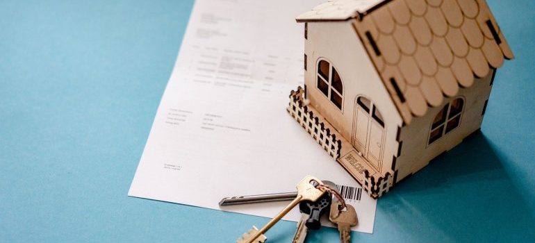 Wooden small home, keys of a home, and a lease paper on the table.