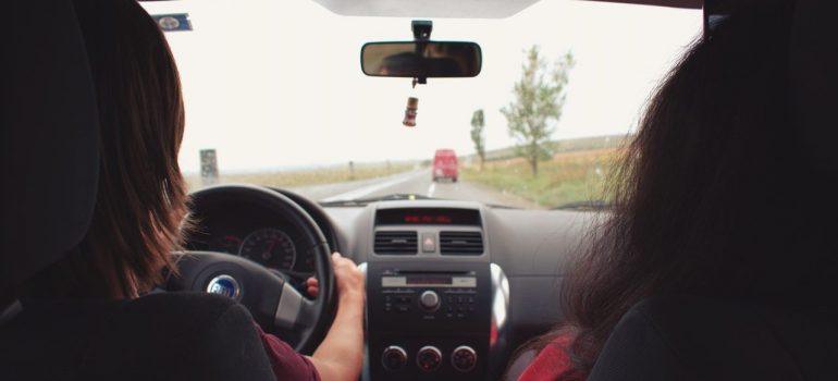 two girls sitting in the front of the car, while one is driving to one of the top 7 moving destinations in the US