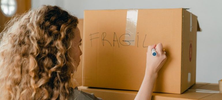 Girl labeling cardboard box with fragile content.