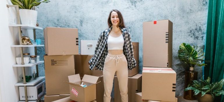 a girl standing beside cardboard boxes, packing for college move-in day