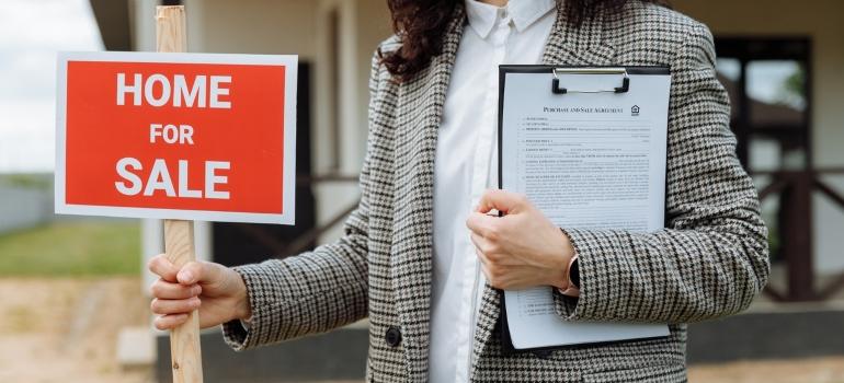 A woman holding a Home for sale sign.