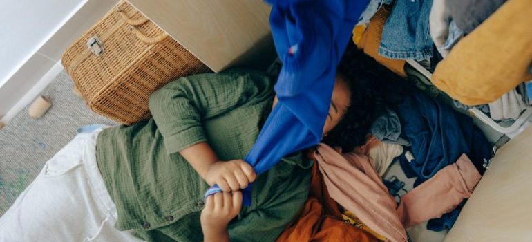 A girl lying on the pile of clothes thinking how to declutter your home before Florida relocation