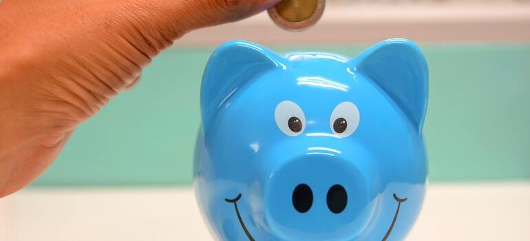 A person putting money inside a blue piggy bank