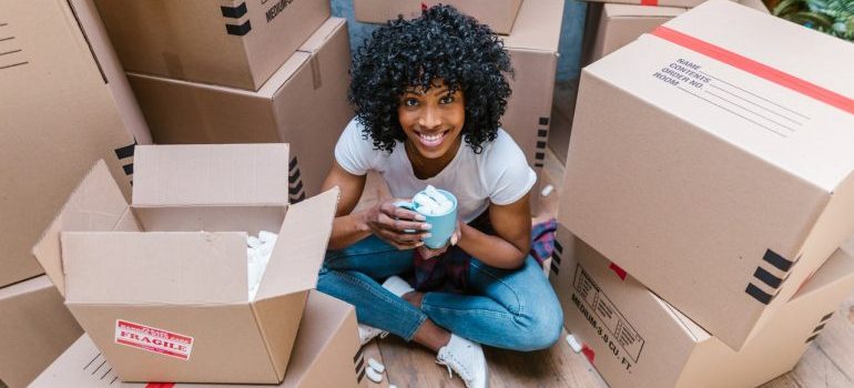 Girl with the cup of coffee sitting between moving boxes