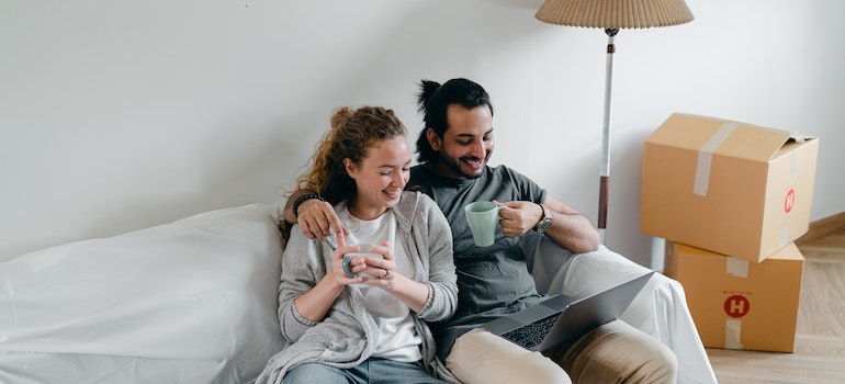 A couple sitting on a couch and drinking coffee with a smile on their faces.