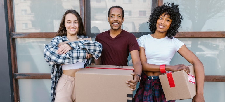 Three friends smiling while holding carton boxes.