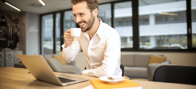 Hombre bebiendo café mientras trabaja en su computadora portátil