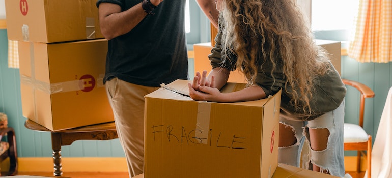 Man, and women talking while she is labeling a box 