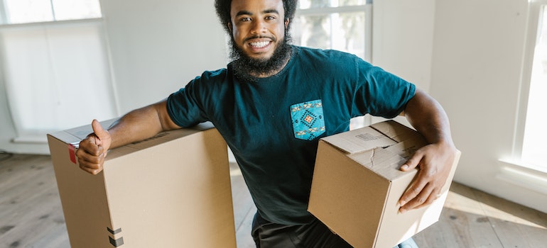 una de las empresas de mudanzas de larga distancia Houston Heights, TX tiene para ofrecer, que sostiene una caja y sonriendo 