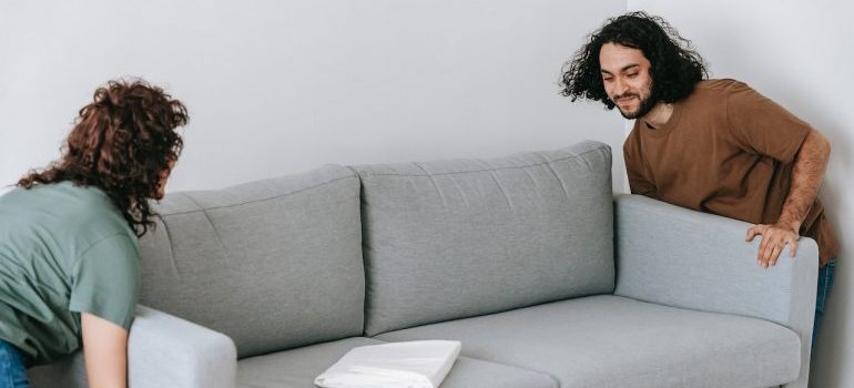 Couple carrying large sofa and talking about items you shouldn't take when moving out of state