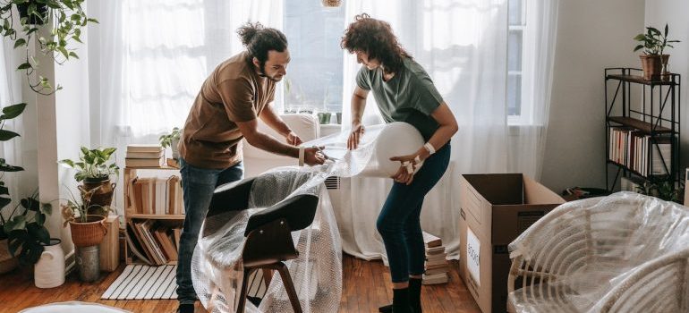 Couple wrapping a chair and preparing store your furniture before moving long distance