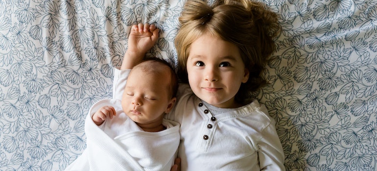 Baby sleeping beside girl on gray floral textile