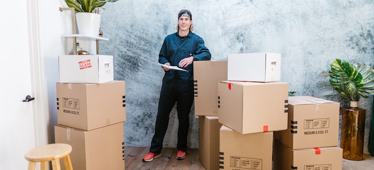 a man standing next to the cardboard boxes ready for moving from Dallas to Miami