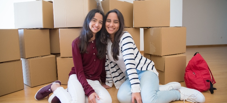two girls sitting in front of the moving boxes 
