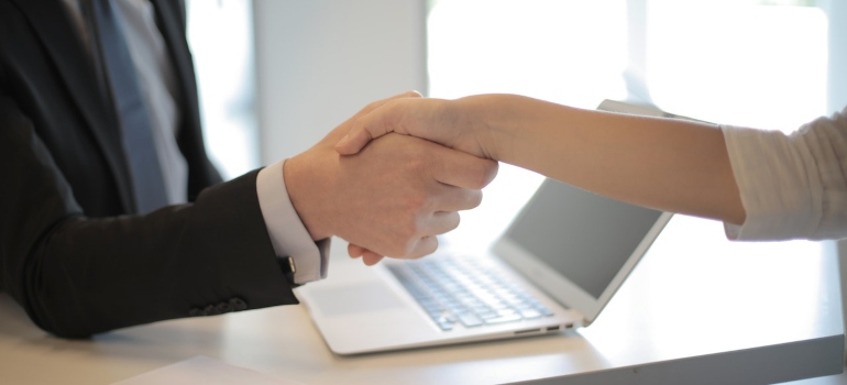 A man in a suit shaking a hand with a woman to confirm a job deal after she was able to choose the best city in TX when moving.