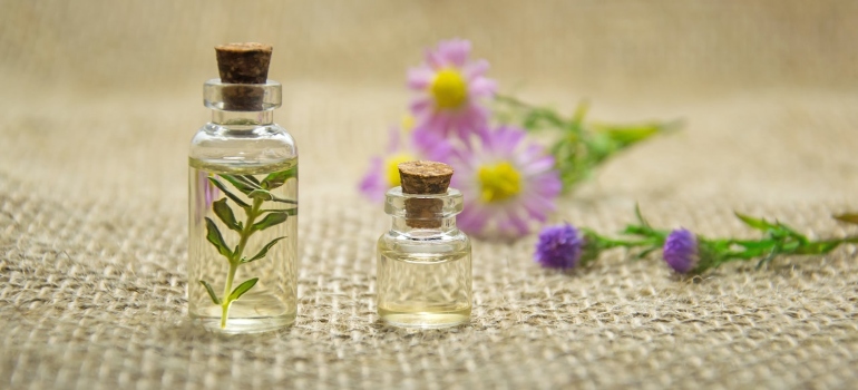 Imagen de dos pequeñas botellas de vidrio junto a flores de color púrpura 