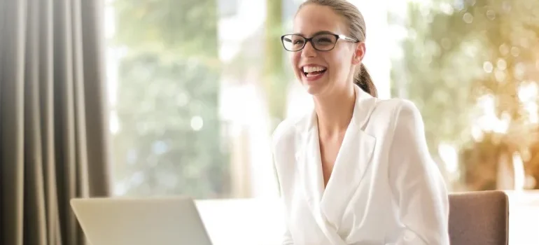 A smiling woman by her laptop, doing research about moving to NYC from Cedar Park