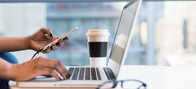 Laptop on table with a hand holding a phone