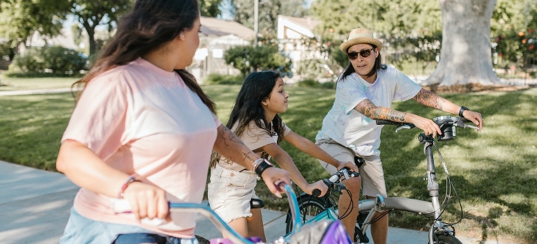 Dos mujeres y una niña en bicicleta en el parque y hablar de la vida en los Suburbios de San Antonio