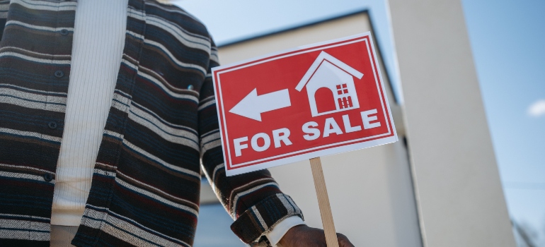 a man holding a "for sale" sign for those wanting to buy a second home in Terrell Hills