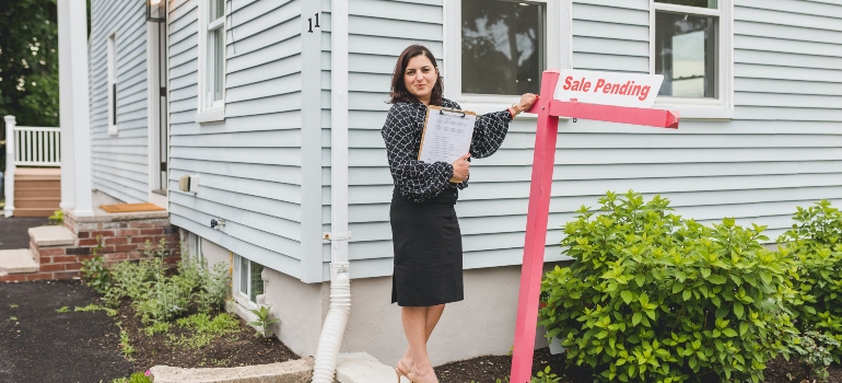 a woman standing next to a "for sale sign"