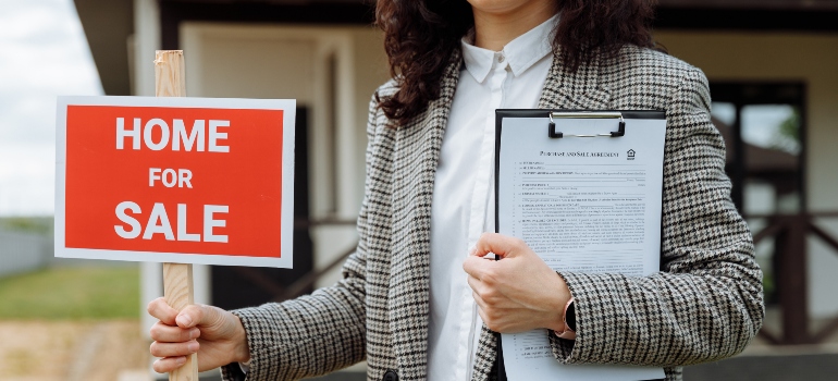 a woman holding a "for sale" sign